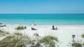 A beach with white sand, a few umbrellas, and a sign.