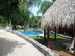 A pool area with a thatched roof structure, surrounded by stone walls and greenery. - Pueblo del Mar 4☙Monkeys & Birds will make your mornings special❧ (Tamarindo)