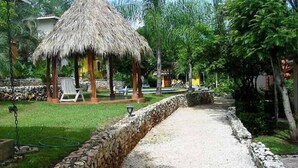 A pathway leading to a thatched-roof gazebo surrounded by lush greenery and a stone wall. - Pueblo del Mar 4☙Monkeys & Birds will make your mornings special❧ (Tamarindo)
