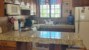 A kitchen with wooden cabinets, a granite countertop, a microwave, a refrigerator, and a window with curtains. - Pueblo del Mar 4☙Monkeys & Birds will make your mornings special❧ (Tamarindo)