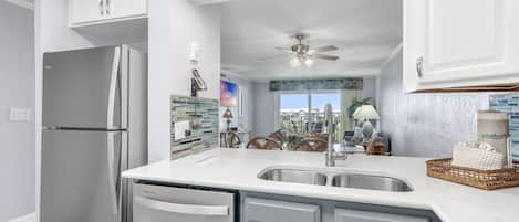 A modern kitchen with a refrigerator, dishwasher, and a large sink.