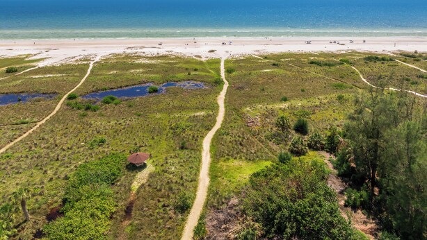 A coastal landscape with a beach, a path through a marshy area, and a small structure with an umbrella. - Steps to Beach. Shared Pool Pet/Family Friendly. Parking Incl. (Siesta Key)