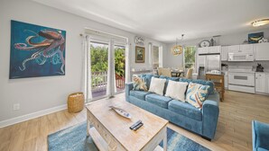 A modern living room with a blue sofa, wooden coffee table, and a painting of an octopus. - Steps to Beach. Shared Pool Pet/Family Friendly. Parking Incl. (Siesta Key)