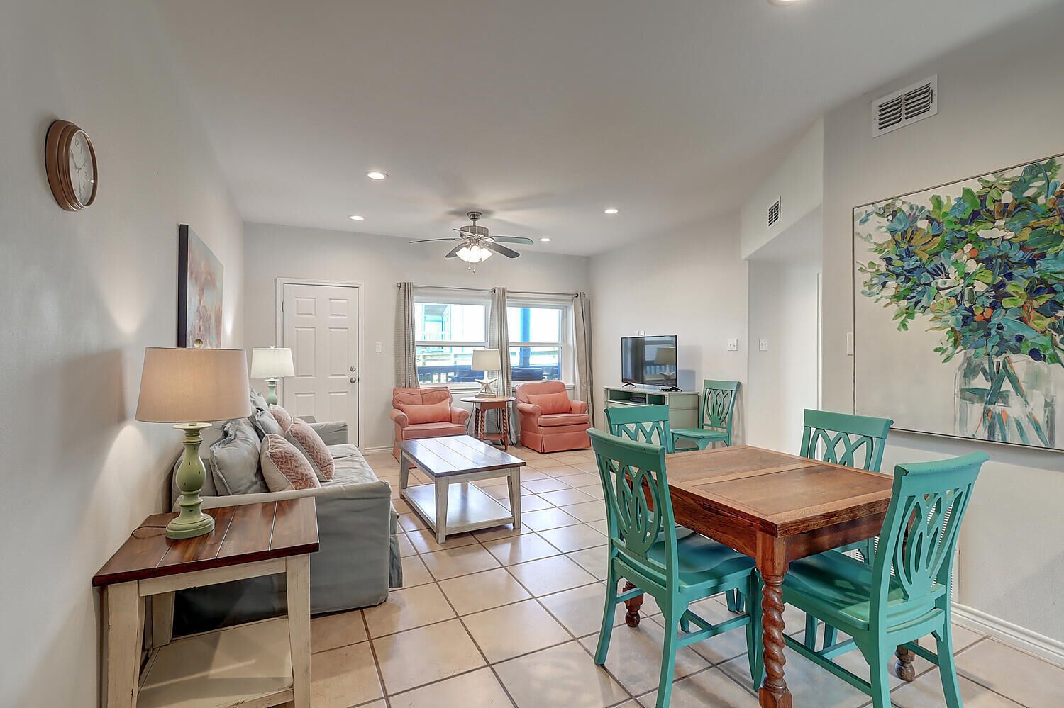 A living room with a sofa, coffee table, and chairs, a dining area with a table and chairs, a TV, and a ceiling fan.
