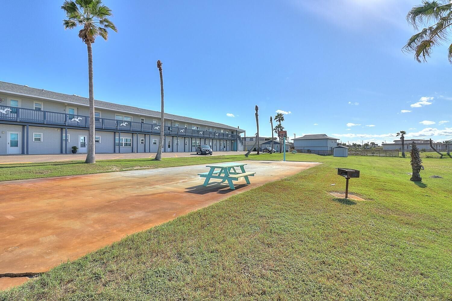 A motel with a parking lot, picnic table, and palm trees.