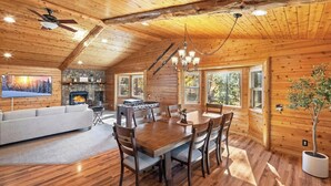 A cozy cabin interior with a dining area, fireplace, and large windows. - Golden Oaks by Destination Big Bear :Luxury Log Cabin w/ Peaceful Setting in High End Neighborhood! Foosball Table/Arcade Game! Gourmet Kitchen! Master Suite w/Private Bathroom! Garage Parking! Propane BBQ! (Big Bear Lake)