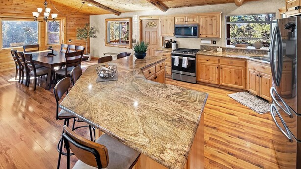 A spacious kitchen with wooden cabinets, a granite island, stainless steel appliances, and a large dining area with a wooden table and chairs. - Golden Oaks by Destination Big Bear :Luxury Log Cabin w/ Peaceful Setting in High End Neighborhood! Foosball Table/Arcade Game! Gourmet Kitchen! Master Suite w/Private Bathroom! Garage Parking! Propane BBQ! (Big Bear Lake)