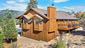 A wooden cabin with a balcony, surrounded by trees and mountains. - Golden Oaks by Destination Big Bear :Luxury Log Cabin w/ Peaceful Setting in High End Neighborhood! Foosball Table/Arcade Game! Gourmet Kitchen! Master Suite w/Private Bathroom! Garage Parking! Propane BBQ! (Big Bear Lake)