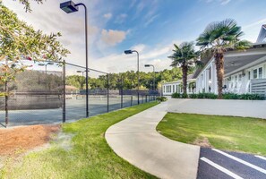 A tennis court with a fence, a pathway, and a building with a white exterior and palm trees. - ParLaMer Wonderful 7BR home in DeBordieu w/ super location, great porches (Georgetown)