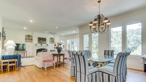 A spacious dining area with a glass table surrounded by striped chairs, a chandelier, and a fireplace.