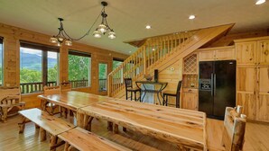 A wooden cabin with a large dining table, benches, a kitchen area, and a staircase leading to an upper level. - Knockin On Heavens Door: Incredible Views, Theater (Gatlinburg)