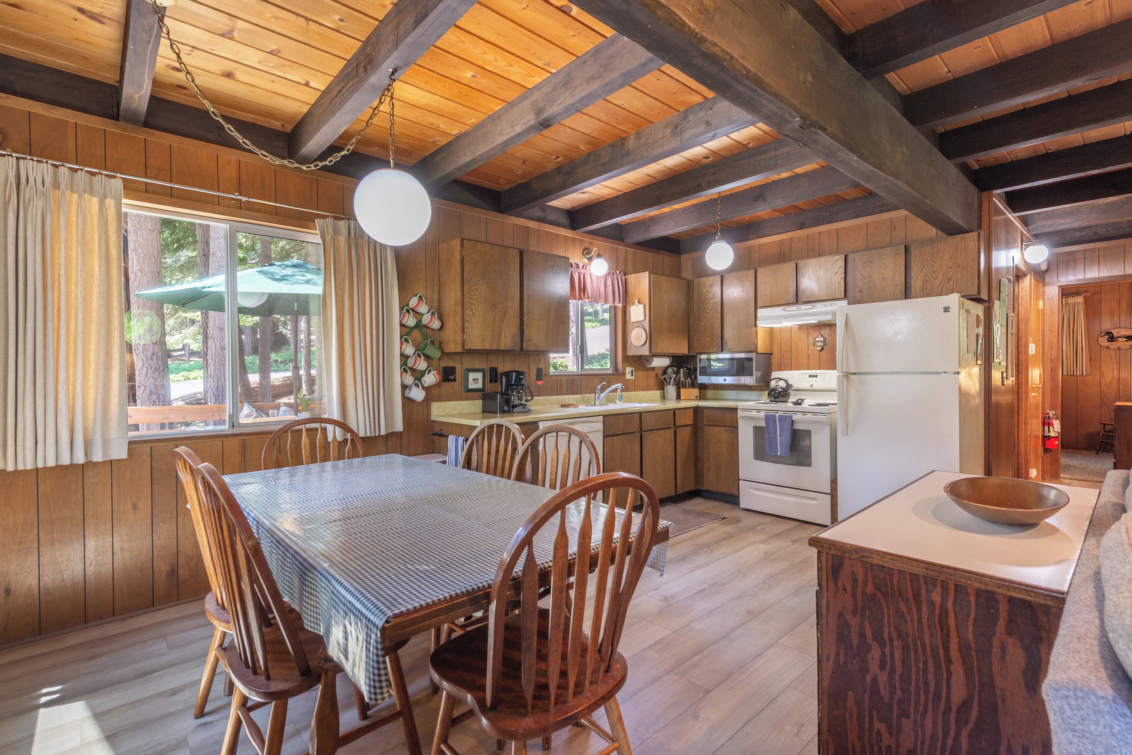 L’intérieur d’un chalet rustique comprend une table à manger en bois, des chaises, une cuisine équipée d’un réfrigérateur, d’une cuisinière et de placards.