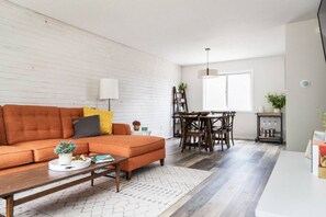 A modern living room with a sofa, coffee table, and dining area with chairs and a chandelier.