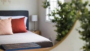 Et soveværelse med seng, sengebord, lampe, et vindue med rullegardiner og et spejl.