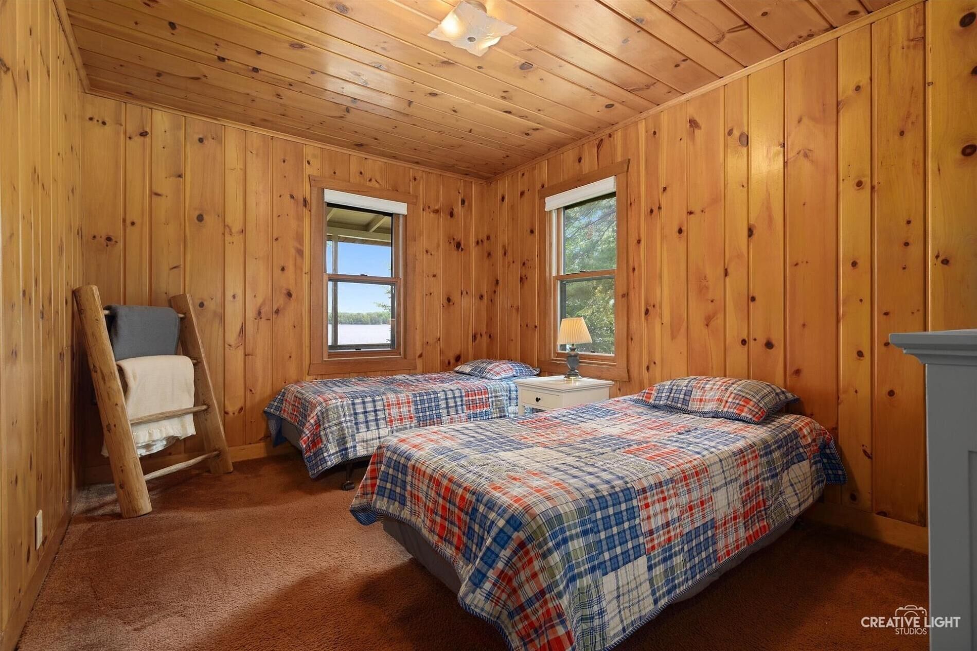 A cozy cabin room with two beds, a wooden ladder, and a window providing a view of the outdoors.