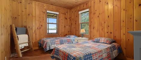 A cozy cabin room with two beds, a wooden ladder, and a window providing a view of the outdoors.