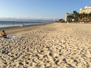 A beach with footprints, a person sitting on a towel, and buildings in the background.