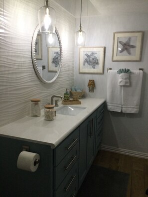 Een badkamer met een witte wastafel, een spiegel en een handdoekhouder. Er hangen prestaties aan de muur en een zeester decoratie.