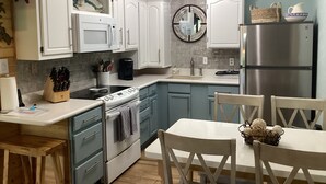Een moderne keuken met witte kasten, een roestvrijstalen koelkast en een eethoek met een witte tafel en stoelen.