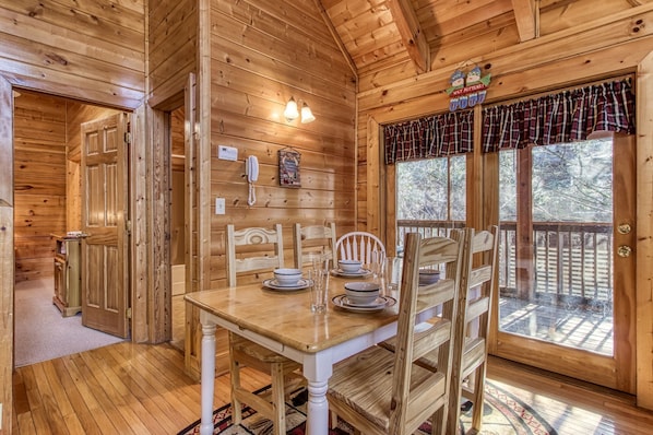 Cozy cabin-style room with a dining table, chair, and bench seat, featuring a wooden ceiling and window with plaid curtains.