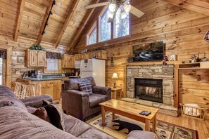 Cozy cabin with a high ceiling, leather sofa, and fireplace in the living area, plus a kitchen with wooden cabinets and stone fireplace.