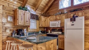 A wooden cabin-style kitchen with wooden cabinets, a granite countertop, a microwave, a refrigerator, and a coffee maker.