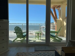 Ein Balkon mit Blick auf den Ozean, ein grüner Stuhl, ein kleiner Tisch und eine Holzkonstruktion.