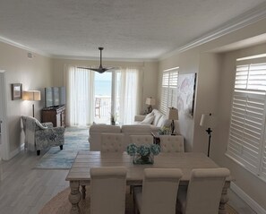 Un salon comprenant un canapé, une table à manger et des chaises, un téléviseur, et donnant sur l’océan grâce à une porte coulissante.