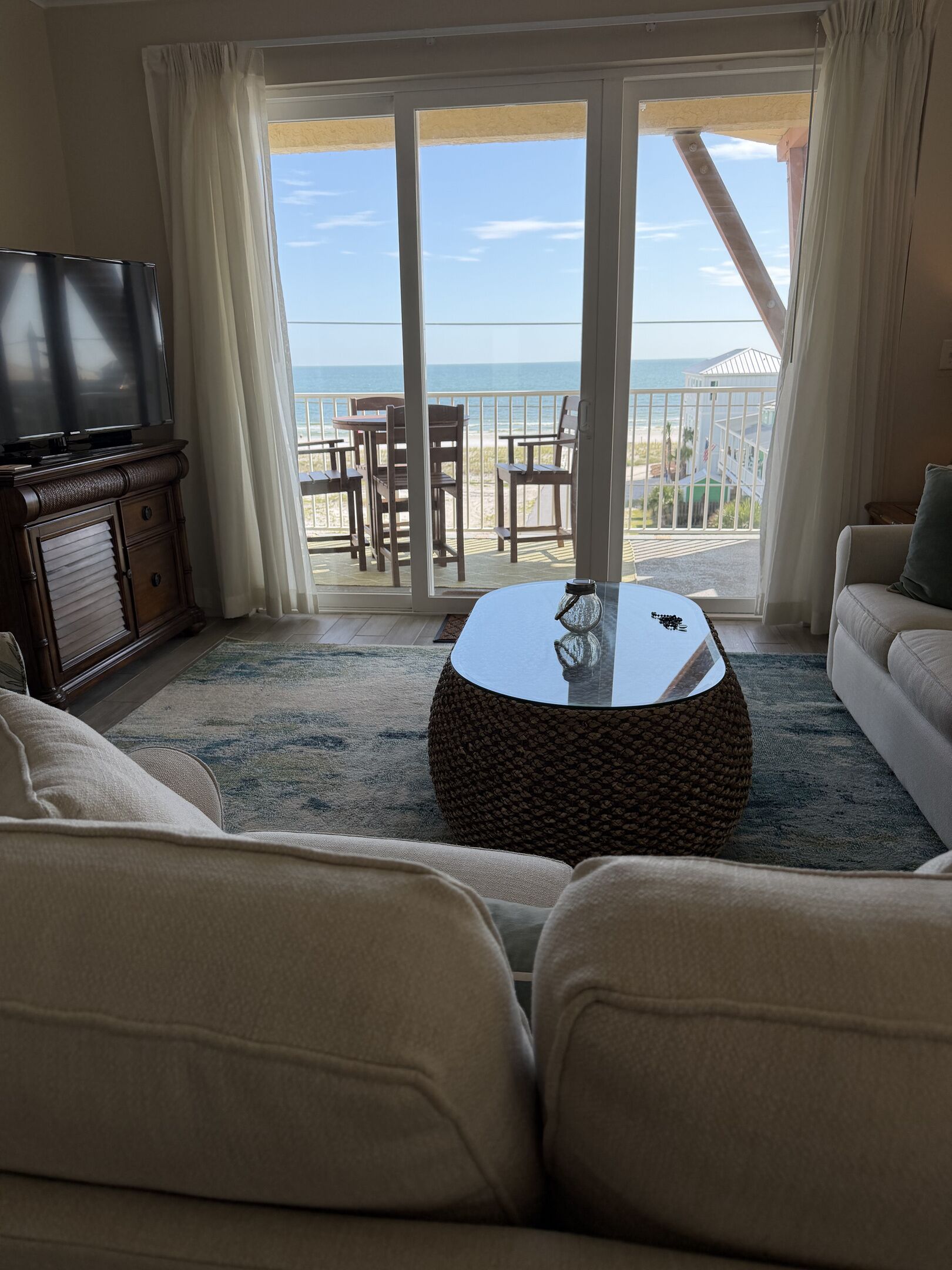 A living room with a television, a round coffee table, and a sofa. There is a balcony with a view of the ocean.