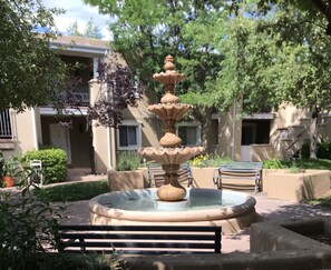 Une fontaine à plusieurs niveaux se trouve dans une cour, avec un banc en premier plan.