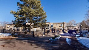A gated residential area with a large tree, a metal gate with a bull sculpture, and a building in the background. - Easy Walk to the Plaza, Gated Retreat, nearby Ski Santa Fe! (Santa Fe)