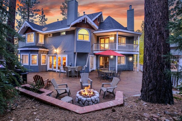 A two-story house with a fire pit in the backyard, outdoor seating, and a large tree.