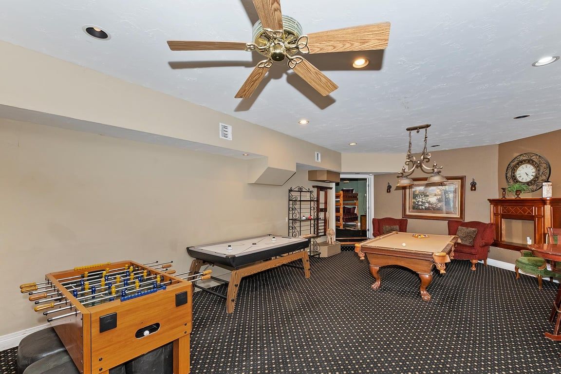 A room with a foosball table, pool table, and a ceiling fan.