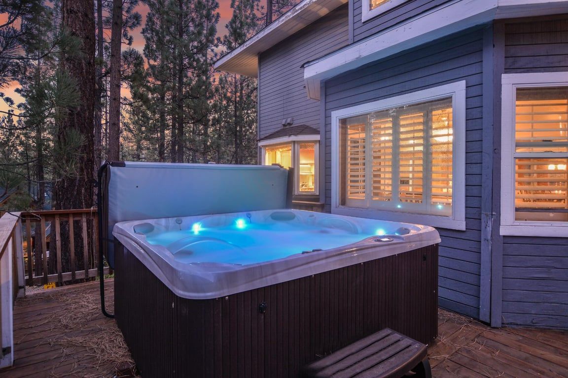 Un bain à remous avec une terrasse en bois et une maison dotée de fenêtres.