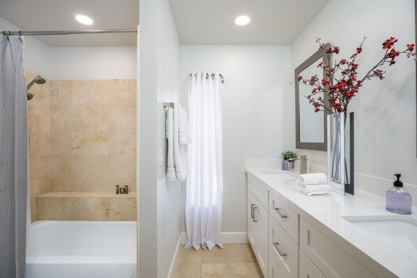 A modern bathroom with a bathtub, shower, white vanity, and a mirror with a vase of flowers.