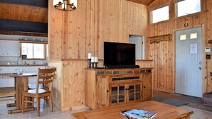 A wooden interior with a TV on a cabinet, a dining area with chairs, and a kitchen with cabinets.