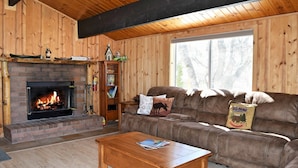 A cozy cabin interior with a fireplace, wooden walls, a leather sofa, and a coffee table.