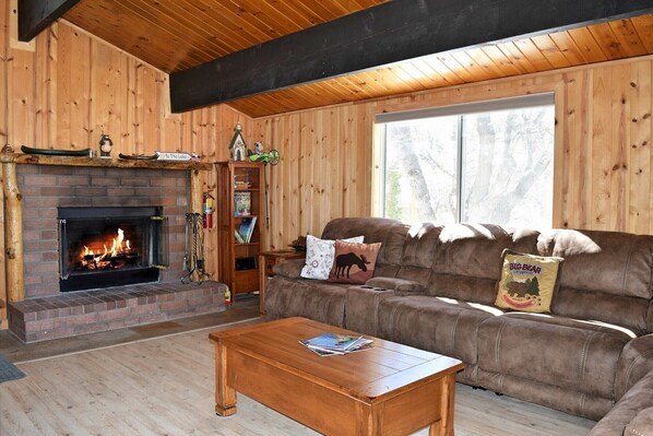 Interior acogedor de una cabaña con chimenea, paredes de madera, un sofá de cuero y una mesita de café.