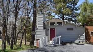 A small, single-story cabin with a red door, a chimney, and a white picket fence.