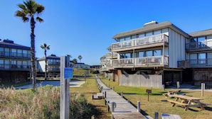 A wooden boardwalk leading to a beachfront hotel with multiple balconies and picnic tables. - Views, swimming pool, boardwalk to the beach, picnic tables, play area, communit (Port Aransas)