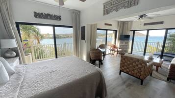 Ein Hotelzimmer mit einem großen Bett, einem Balkon mit Meerblick, einer Essecke mit Stühlen und einem Deckenventilator.