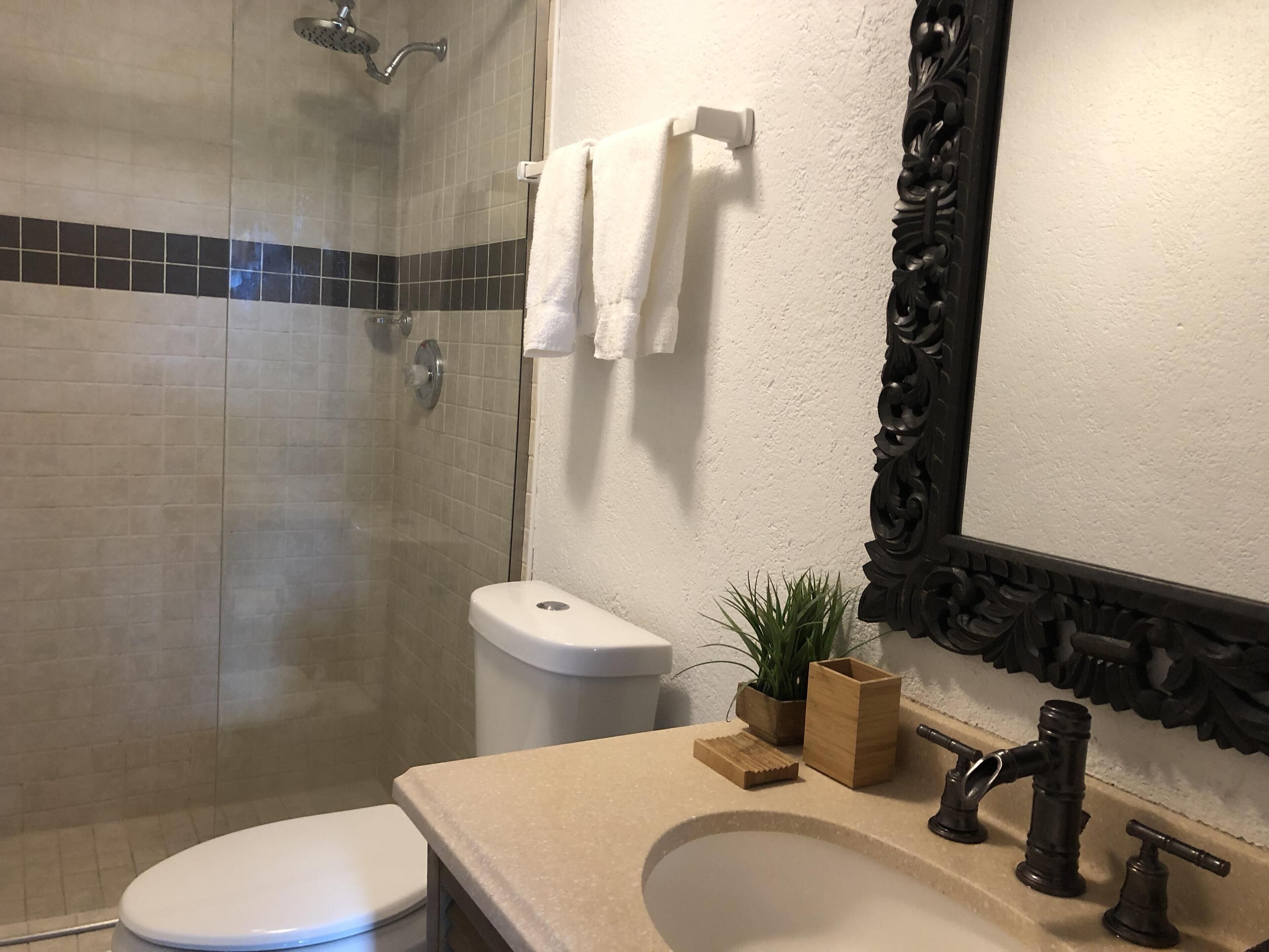 Un baño con ducha, inodoro, lavabo y espejo con un marco decorativo.