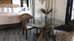 Quarto de hotel com cama, mesa de vidro e cadeiras, um vaso decorativo e um espelho na parede.