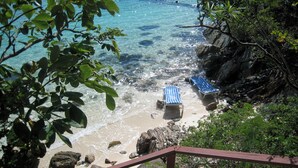 Uma praia com águas cristalinas, duas cadeiras de praia listradas e terreno rochoso.