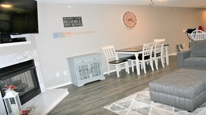 A living room with a fireplace, a dining table with chairs, a clock, and a television.