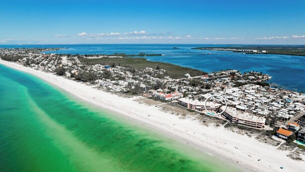 An aerial view of a coastal resort with beachfront properties, a pier, and clear blue waters.