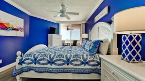 A bedroom with a bed, a nightstand, a ceiling fan, a window, and a view of the outdoors.