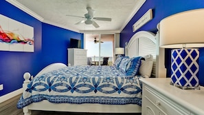Quarto com cama, mesa de cabeceira, ventilador de teto, janela e vista para o exterior.