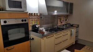 Cocina compacta con microondas, horno y estufa a gas. Hay armarios, un lavabo y diversos utensilios de cocina.
