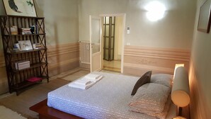Un dormitorio con cama, mesita de noche, estantería y puerta que da al baño.